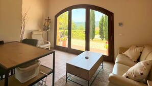 A living room with a sofa, a coffee table, a dining table, and a view through a glass door to an outdoor area. - Annex House with Pool   InBorgo (MONTECASTRILLI)
