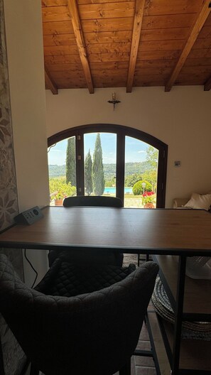 Une pièce avec un plafond en bois, une table et une vue sur un jardin, visible à travers une grande fenêtre en arc de cercle.