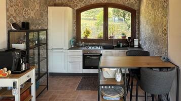 A compact kitchen with a stove, oven, and sink, a dining table with chairs, and a window with a view of greenery.