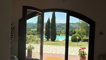 A room with a wooden ceiling, a large sliding glass door leading to an outdoor area with a pool and greenery.