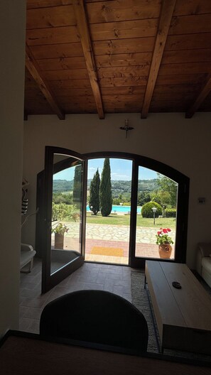 Quarto com teto de madeira, uma grande porta de correr de vidro que dá para área externa com piscina e vegetação.
