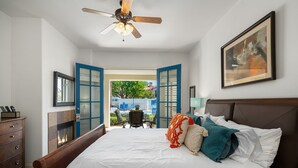 Une chambre à coucher comprenant un lit, un ventilateur de plafond, une cheminée, un bureau avec une chaise et une vue sur l’extérieur.