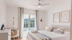 Una camera da letto con un letto, una scrivania, una sedia, una ventola a soffitto e vista sull'esterno.