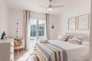 Ein Schlafzimmer mit Bett, Schreibtisch, Stuhl, Deckenventilator und Blick ins Freie.