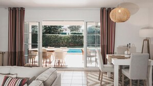 Una moderna camera d'albergo con divano, tavolo da pranzo, sedie e vista su una piscina.