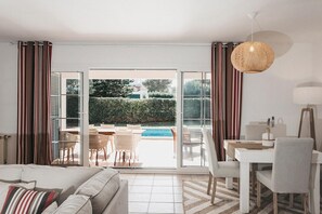 Ein modernes Hotelzimmer mit Sofa, Esstisch, Stühlen und Blick auf einen Pool.