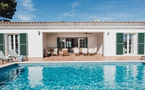 Ein Schwimmbad mit Terrassenbereich, Gartenmöbeln und einem Gebäude mit grünen Fensterläden.