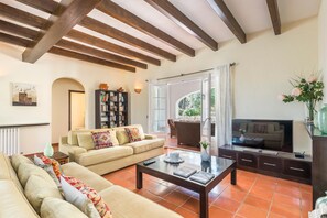 Un salón con sofá, mesa de centro, televisor, estantería y puerta que da a un balcón.