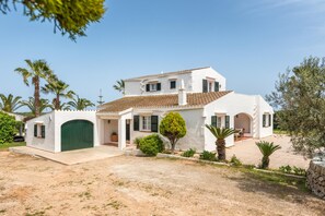 Una villa blanca con techo de tejas, puerta de garaje verde y un pequeño jardín con palmeras.