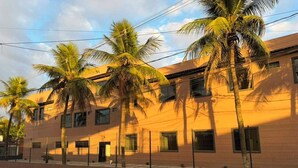 A building with multiple windows, a fence, and palm trees. - Hotel Betel 3 pontes (Itaboraí)