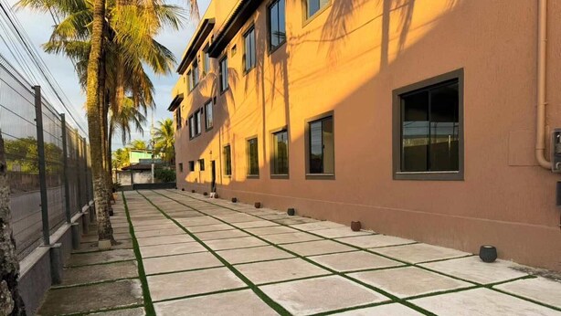 A building with a long, narrow courtyard with a tiled floor and green grass borders. - Hotel Betel 3 pontes (Itaboraí)