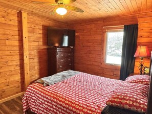 Une chambre dans un chalet en bois, avec un lit, une commode, une télévision et une fenêtre avec des rideaux.
