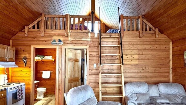 En hytte med sovehems på loftet, et køkken, et badeværelse og en opholdsstue med sofa og stol.