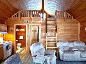 A cabin interior with a kitchen, a dining area, a sofa, and a staircase to an upper level.