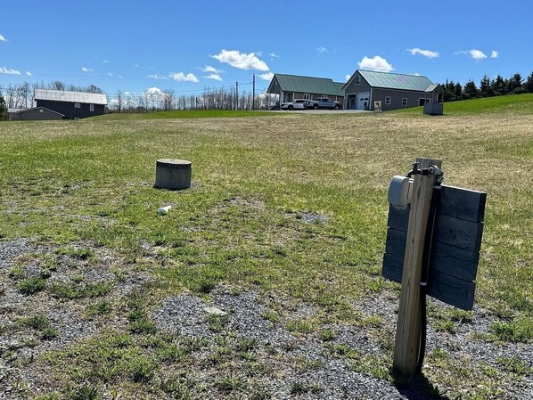 A rural landscape with a gravel field, a wooden post with a sign, and a building with a green roof in the background.