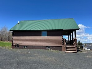 A log cabin with a green roof, a front porch, and a small window.
