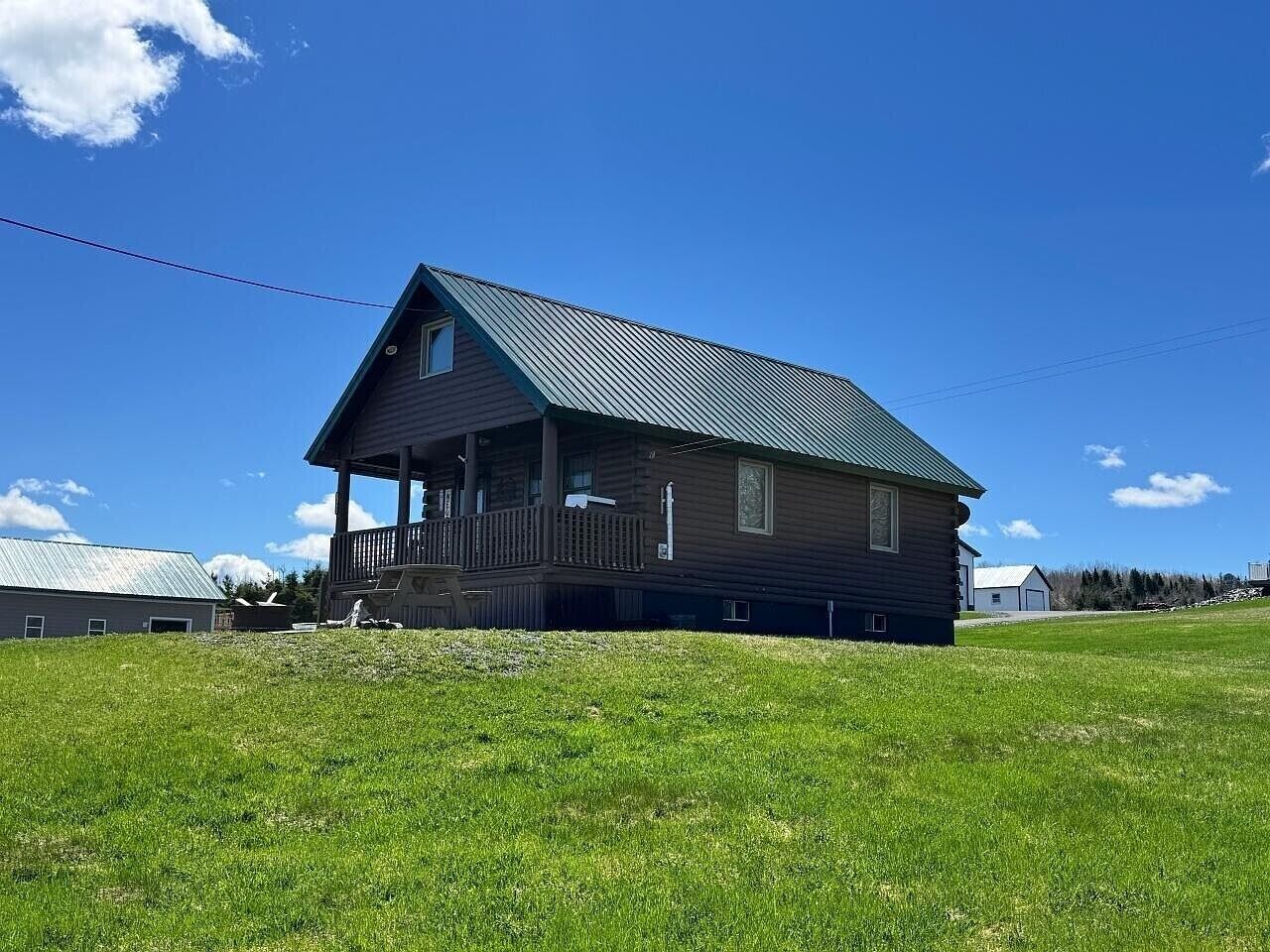 A single-story wooden house with a porch, a metal roof, and a grassy yard.