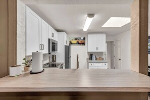 A modern kitchen with white cabinets, a central island, a ceiling light, and a wall-mounted picture of a car.