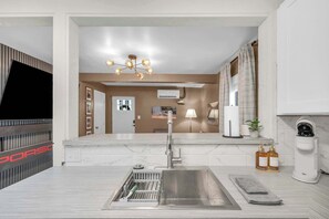 A modern kitchen with a stainless steel sink, a built-in dishwasher, a hanging light fixture, and a large mirror above the sink.