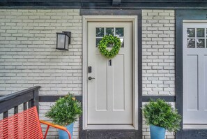A white door with a heart-shaped wreath, a potted plant, and a red chair outside.