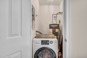 A compact laundry room with a front-loading washer and dryer, a water heater, and a towel rack.