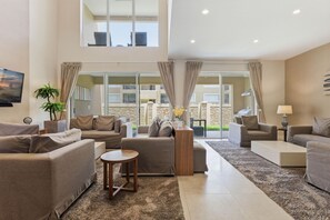 Un salon spacieux avec un plafond haut, de grandes fenêtres et une vue sur l’extérieur.