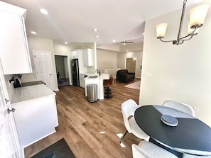 A modern kitchen with white cabinets, a central island, and a dining area with a black table and white chairs. - Atlanta Home: 2-Tier Deck & Wooded Views (Lithia Springs)