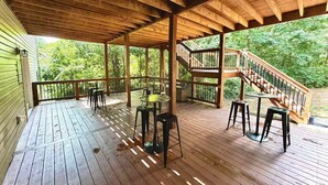 Una terraza de madera con mobiliario exterior, una escalera y vistas a zonas verdes.