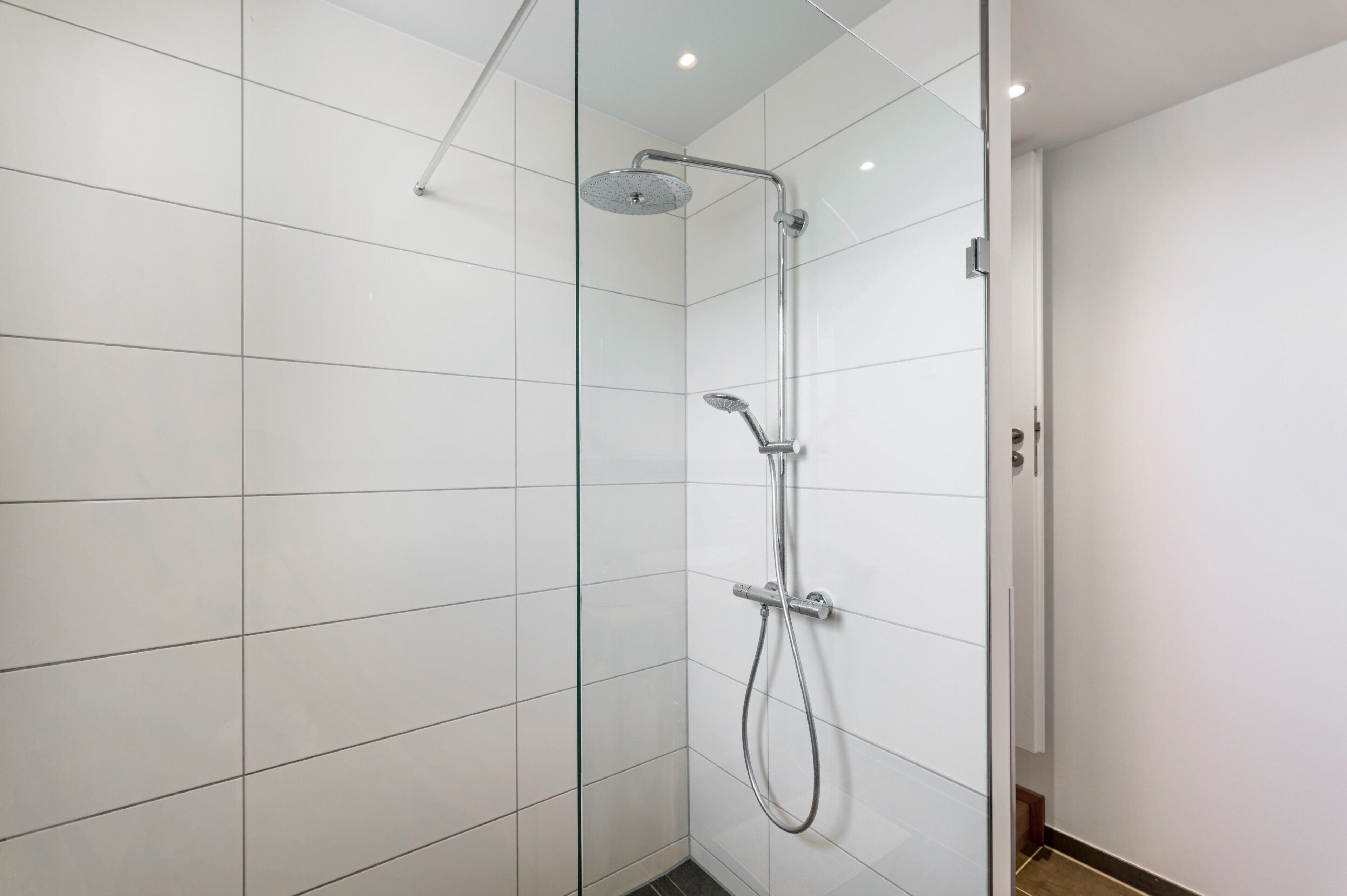 Ein modernes Badezimmer mit weißen Fliesen, einer Duschkabine aus Glas und einer Handbrause.
