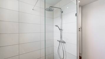 Une salle de bain moderne avec des murs recouverts de carreaux blancs, une douche en verre et un pommeau de douche à main.