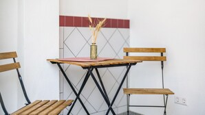 Un tavolino con un vaso di spighe di grano, due sedie di legno e un muro piastrellato con un motivo geometrico.