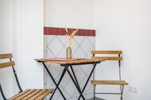 Et lille bord med en vase fyldt med kornaks, to træstole og en flisevæg med et geometrisk mønster.