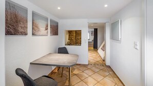 Una zona pranzo con tavolo e sedie, un corridoio con pavimento piastrellato e opere d'arte incorniciate alle pareti.