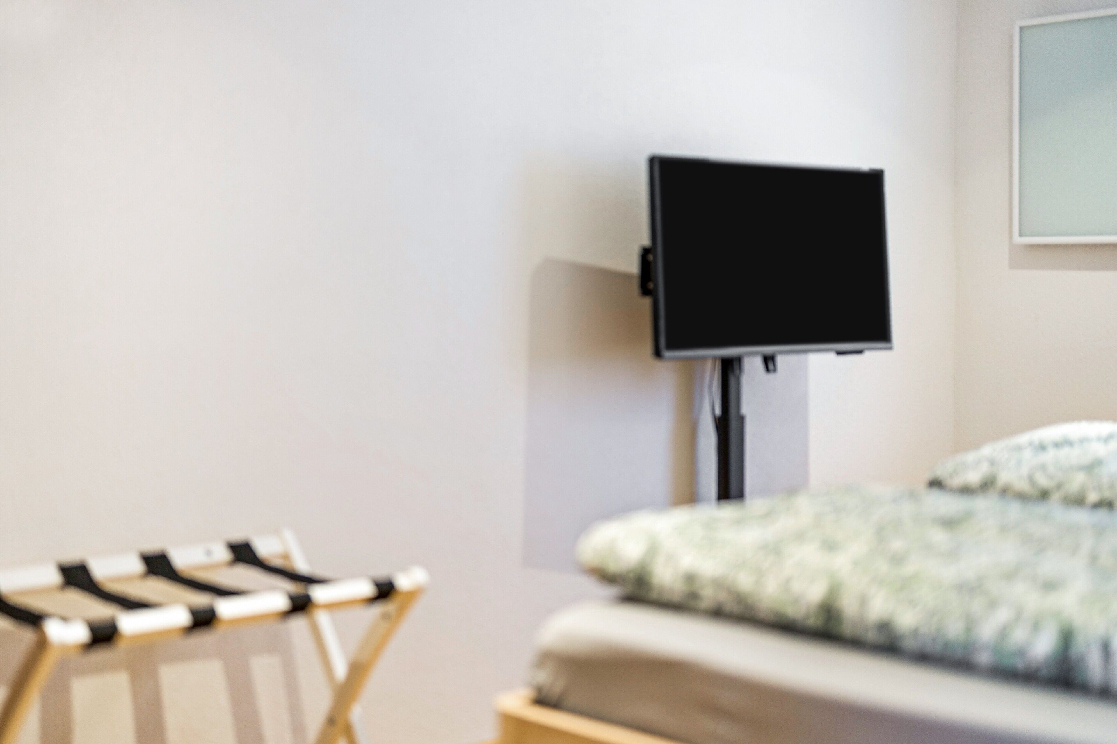 Une chambre avec un lit, un téléviseur fixé au mur et une chaise pliante.
