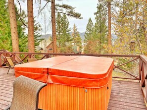 Ein Whirlpool auf einer Holzterrasse mit Blick auf Bäume und ein Haus im Hintergrund.