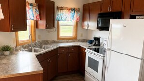 Una cocina con armarios de madera, un refrigerador blanco, una estufa, un microondas y una ventana con cortinas.