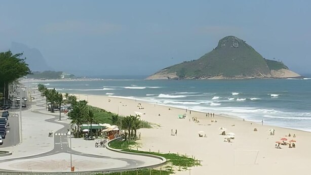 Ein Strand mit einer gewundenen Straße, Palmen und einem Hügel mit einem Denkmal.