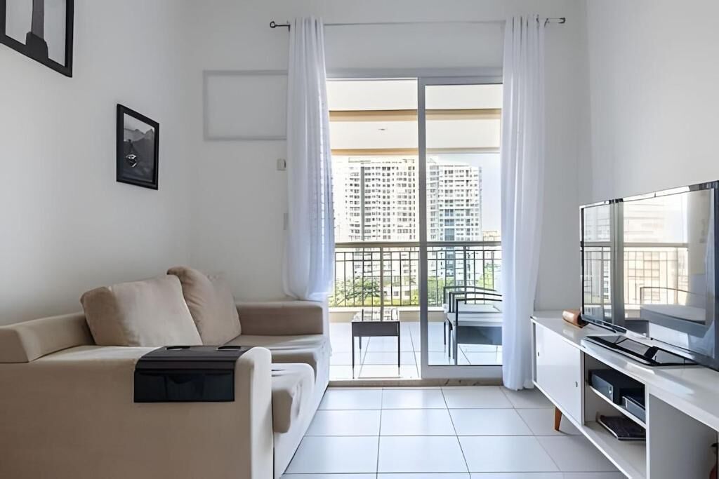 Un salon moderne avec un canapé, un téléviseur à écran plat et un balcon offrant une vue sur la ville.