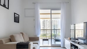 Ein modernes Wohnzimmer mit einer Couch, einem Flachbildfernseher und einem Balkon mit Blick auf die Stadt.