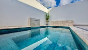Une piscine d’un bleu éclatant, bordée de carreaux, entourée de murs blancs et agrémentée d’une petite plante en pot.