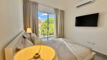 A bedroom with a bed, a TV, an air conditioner, and a window with curtains.