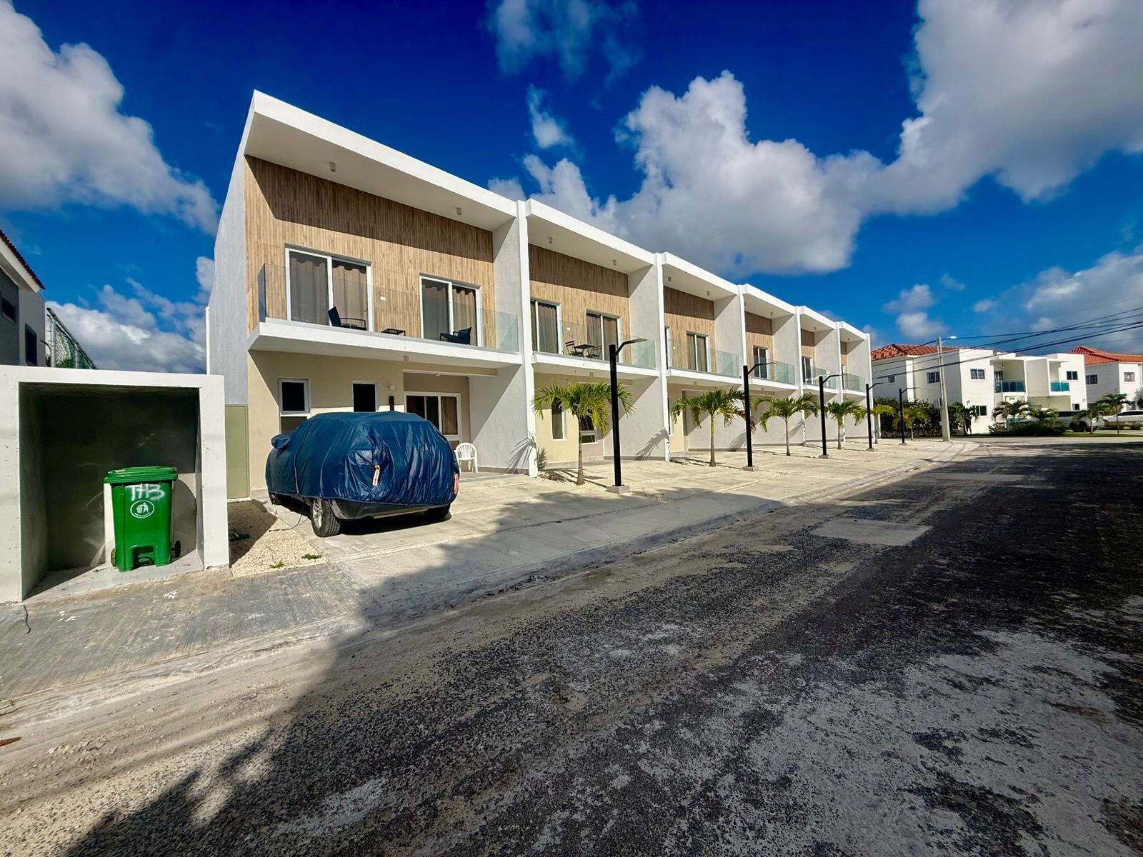 A modern multi-story residential building with a flat roof, large windows, and a covered parking area.