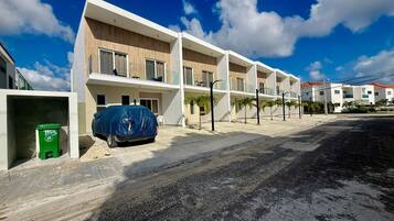 A modern multi-story residential building with a flat roof, large windows, and a covered parking area.
