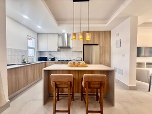 Une cuisine moderne avec des meubles en bois, un îlot central doté de tabourets de bar et un éclairage suspendu.