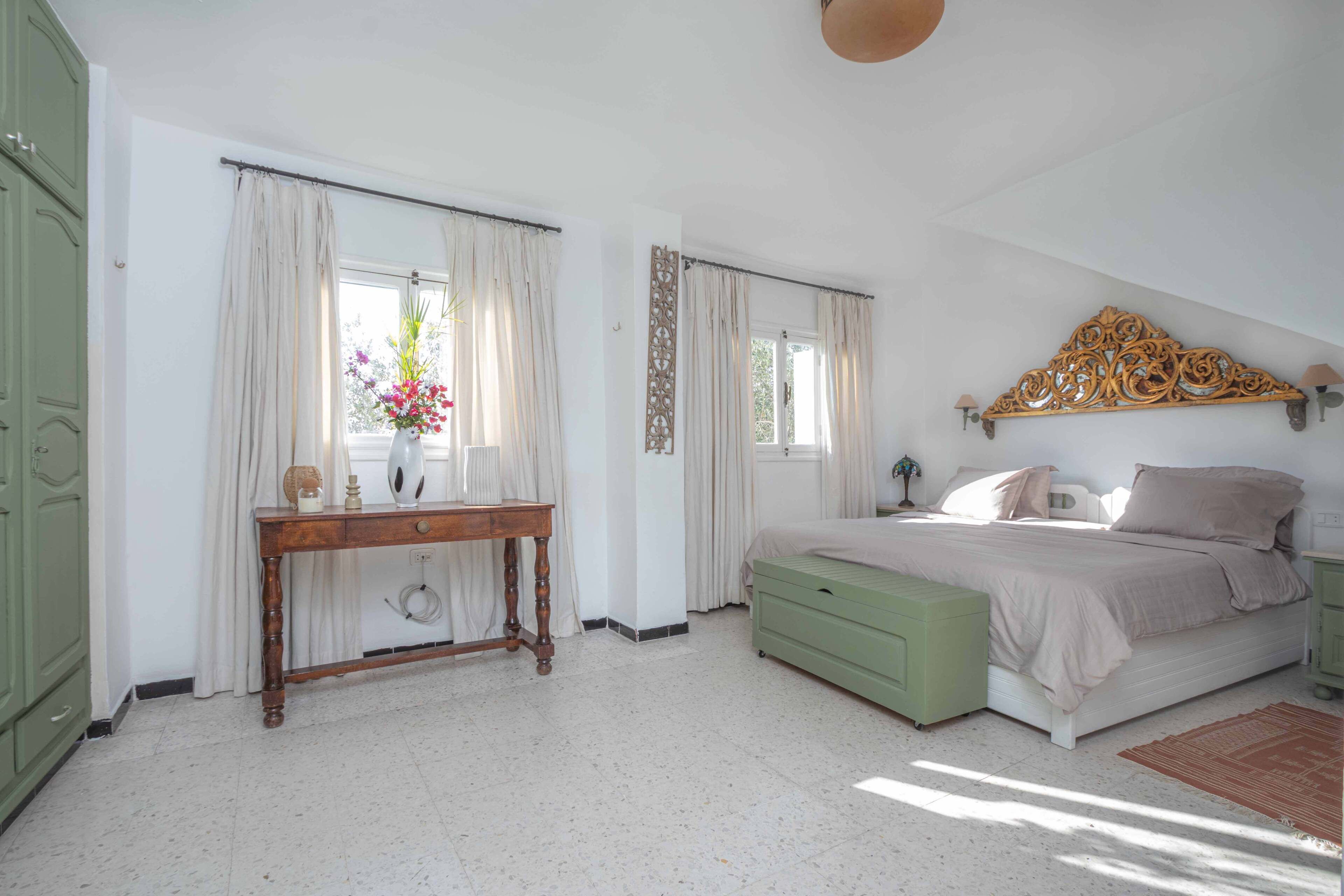 A bedroom with a bed, a bedside table, a dresser, and a window with curtains.