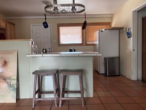 A kitchen with a central island, a refrigerator, a window with blinds, and a door. - North Valley Charmer (Albuquerque)