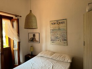Ein Schlafzimmer mit einem Bett, einer Hängeleuchte, einem Poster des Magazins The New Yorker und einem Fenster mit Vorhängen.