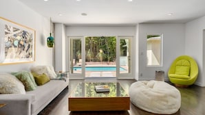 Ein modernes Wohnzimmer mit Blick auf einen Pool, ein weißes Sofa, ein grüner Sessel und ein Glastisch.
