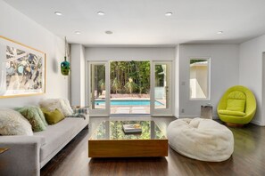 Ein modernes Wohnzimmer mit Blick auf einen Pool, ein weißes Sofa, ein grüner Sessel und ein Glastisch.