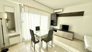 A modern hotel room with a dining area, a flat-screen TV, and a large window with curtains. - Antibes - Studio for 2 people - Parking - Swimming pool - Air conditioning (Antibes)
